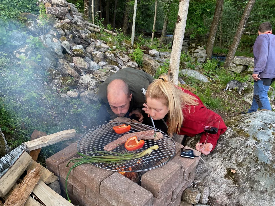 Två personer hjälps åt vid en grill i skogen.